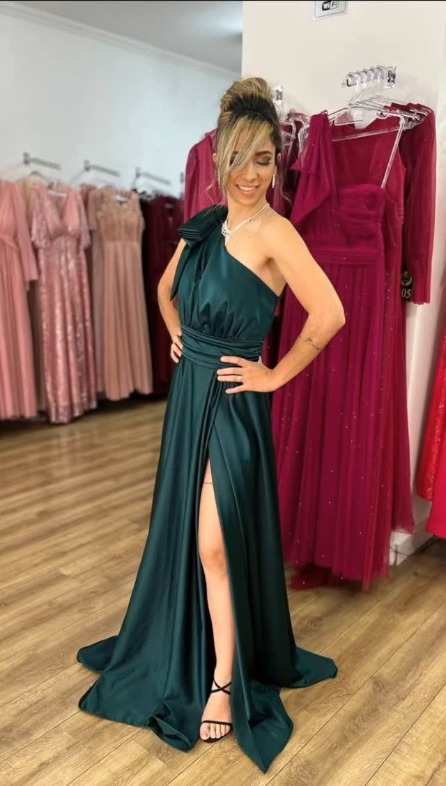 Cliente experimentando vestido verde na loja, com outros modelos do acervo ao fundo